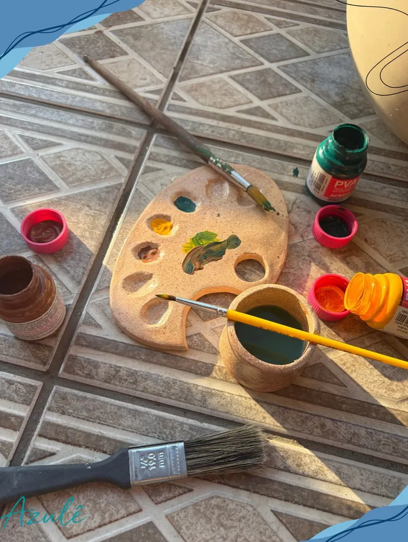 Paleta de cerâmica fria com tintas misturadas, potinho de água e pincéis